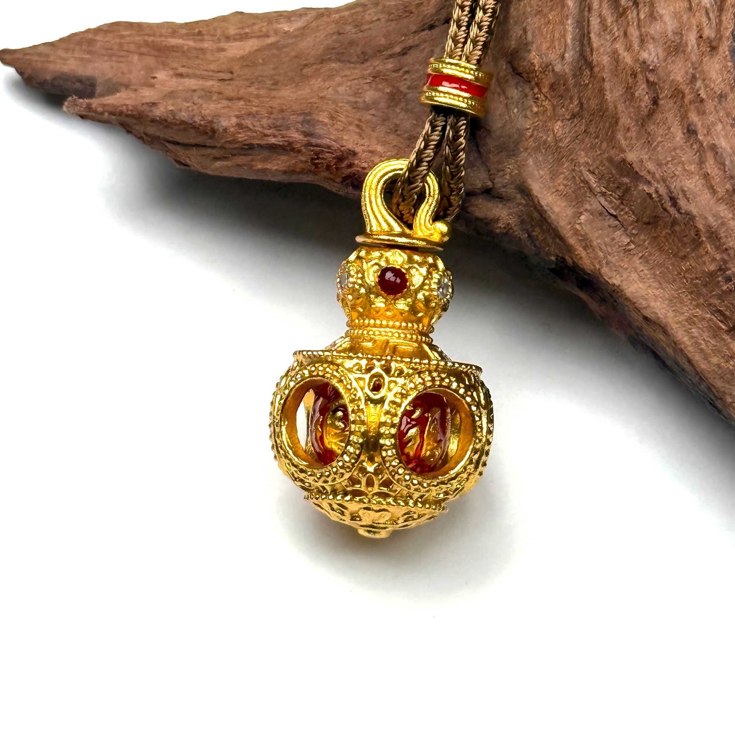 Macro shot of a sand gold filigree prayer gourd necklace on wood, capturing the precise red enamel core inside the hollow globe.
