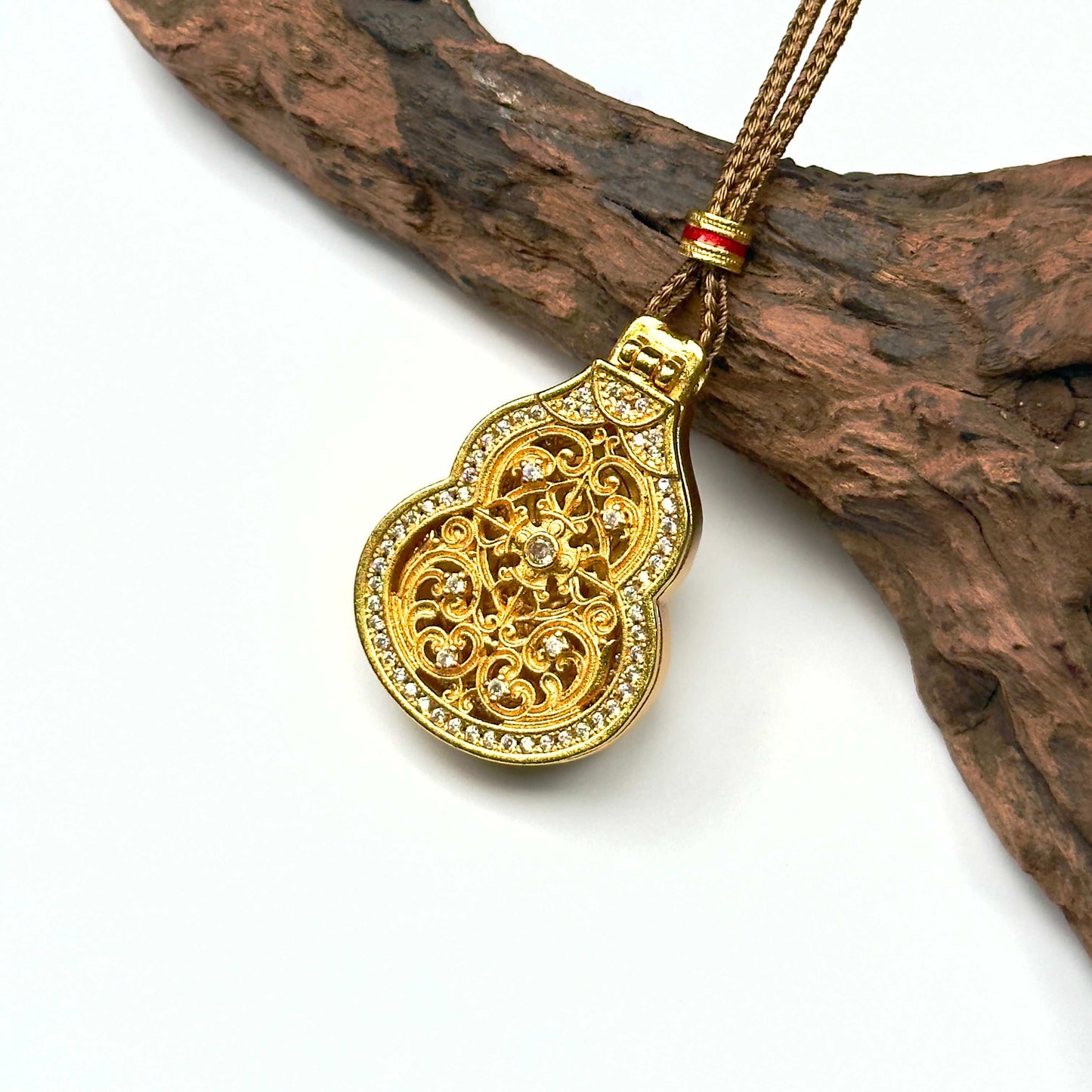 A regal sand gold filigree Hulu locket protective amulet adorned with pavé rhinestones, resting elegantly against a rustic driftwood branch.