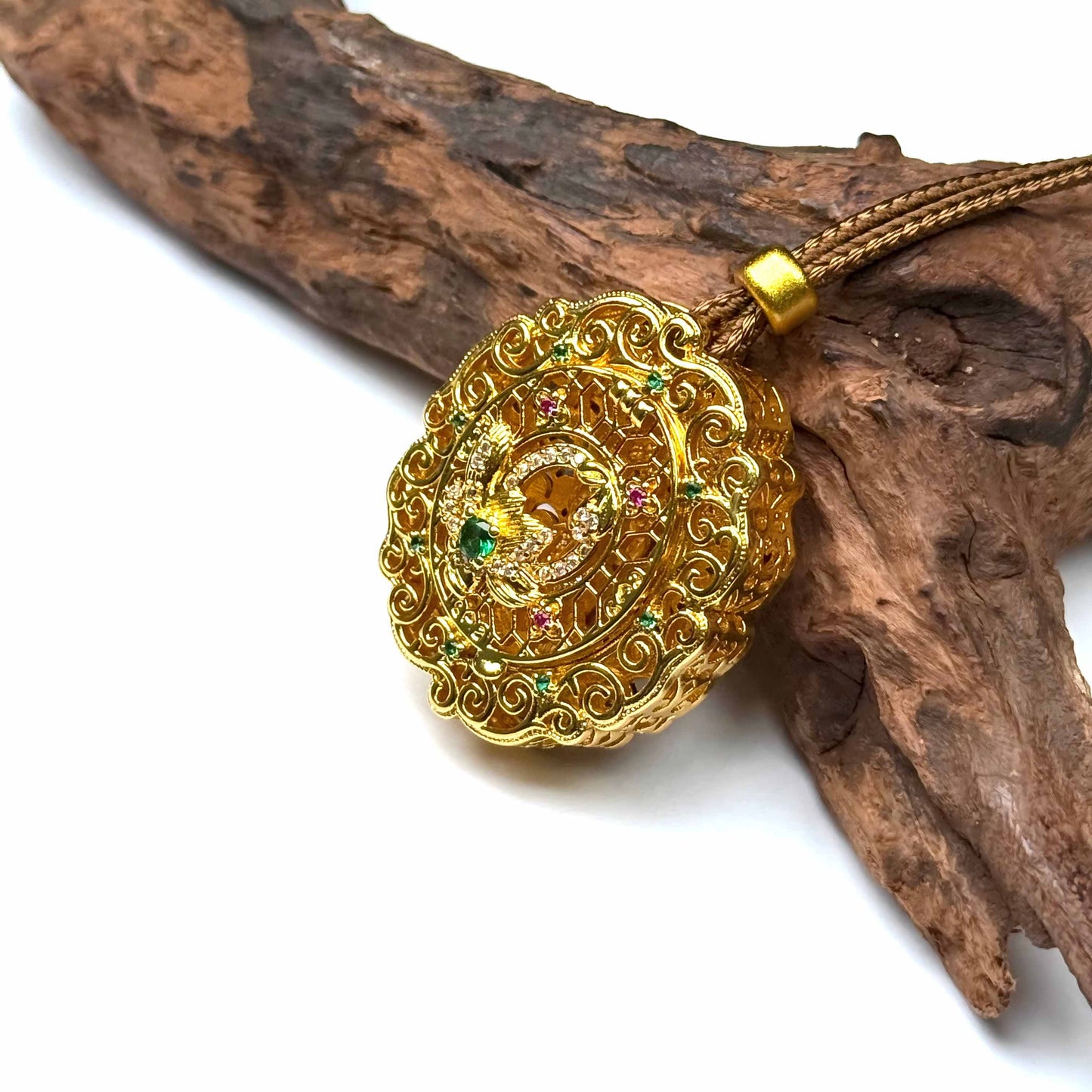 A luxurious circular sand gold Gau box amulet pendant decorated with gemstones, resting elegantly against natural rustic wood.