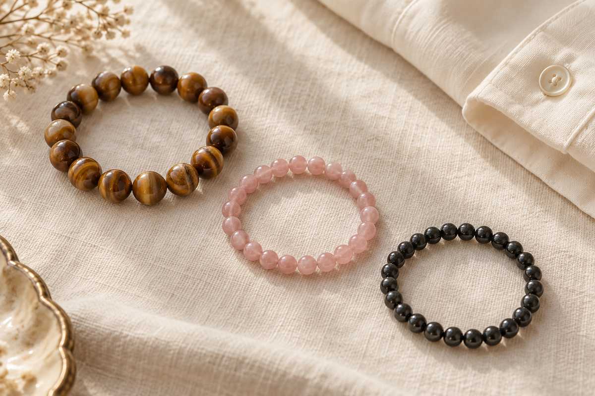 Golden-brown, soft pink, and charcoal beaded bracelets arranged separately on ivory linen.