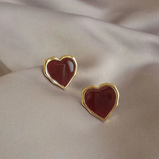 Gold-tone 925 sterling silver red heart stud earrings displayed on satin fabric