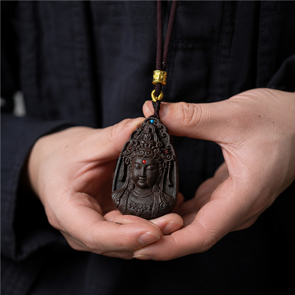 Lifestyle view of a person holding an agarwood Guanyin pendant necklace