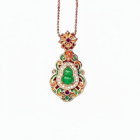 A crisp front view of an authentic sand gold Hulu gourd pendant featuring a central translucent green chalcedony stone, colorful enamel leaf motifs, and a brilliant rhinestone border on a white background.