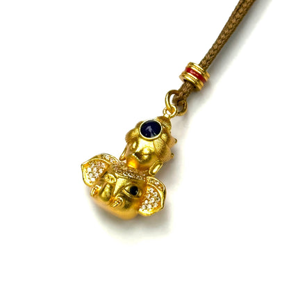 An angled view of a golden Lord Ganesha amulet necklace, showcasing the micro-pave crystal ears, blue crown stone, and detailed trunk.