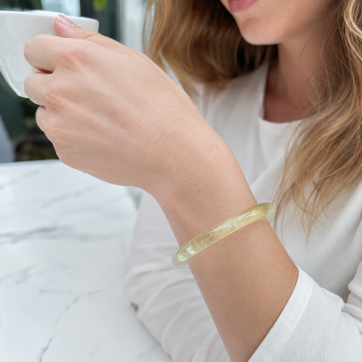 Yellow citrine bangle worn on wrist while holding a white cup