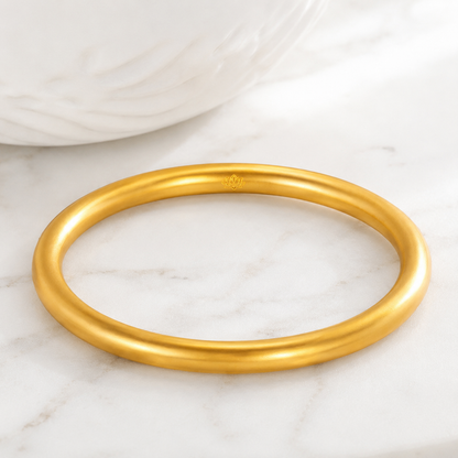Smooth gold-tone sandgold bangle on white marble surface