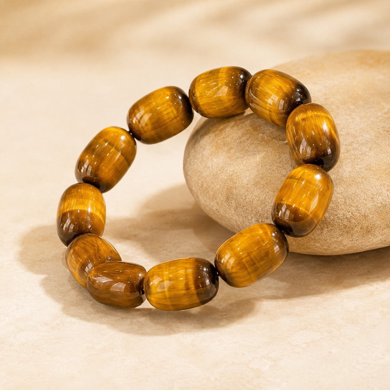 Golden tiger’s eye barrel bead bracelet displayed beside a smooth stone