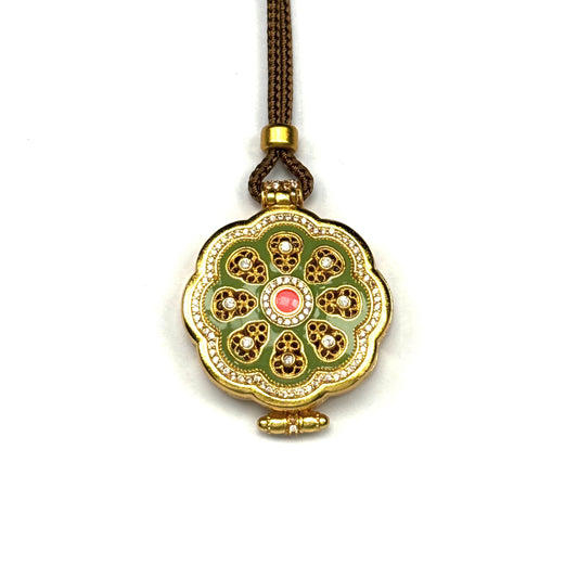 A beautiful closed gold-tone locket pendant featuring green enamel, sparkling rhinestones, and a pink center stone, displayed on a pure white background.