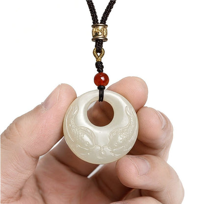 Hetian jade double fish pendant held in hand, showing the paired fish carving