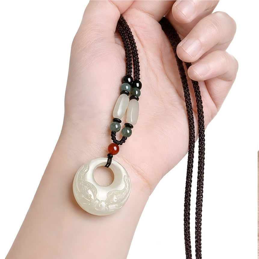 Hetian jade double fish pendant held in hand, showing the necklace cord and scale