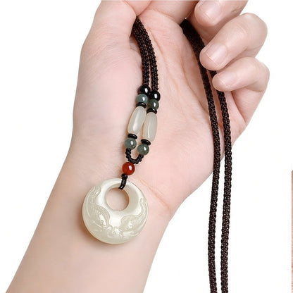 Hetian jade double fish pendant held in hand, showing the necklace cord and scale