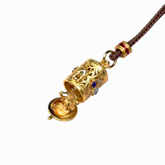A front open view of the sand gold cylindrical capsule necklace, showcasing the bottom lid flipped down to reveal a hidden golden seated deity statue inside.