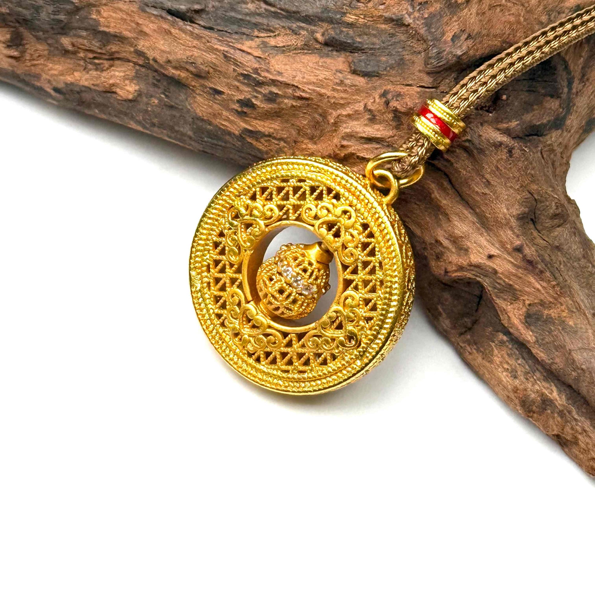 Macro top-down detail of the engraved gold filigree back side of a round spinner pendant necklace resting against natural rustic wood.