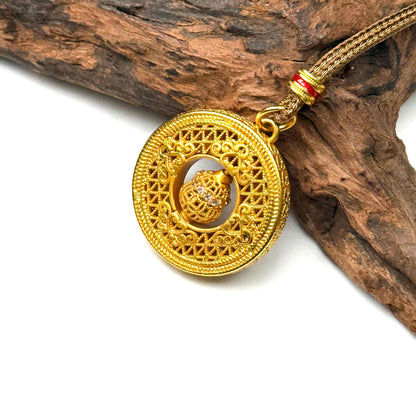 Macro top-down detail of the engraved gold filigree back side of a round spinner pendant necklace resting against natural rustic wood.
