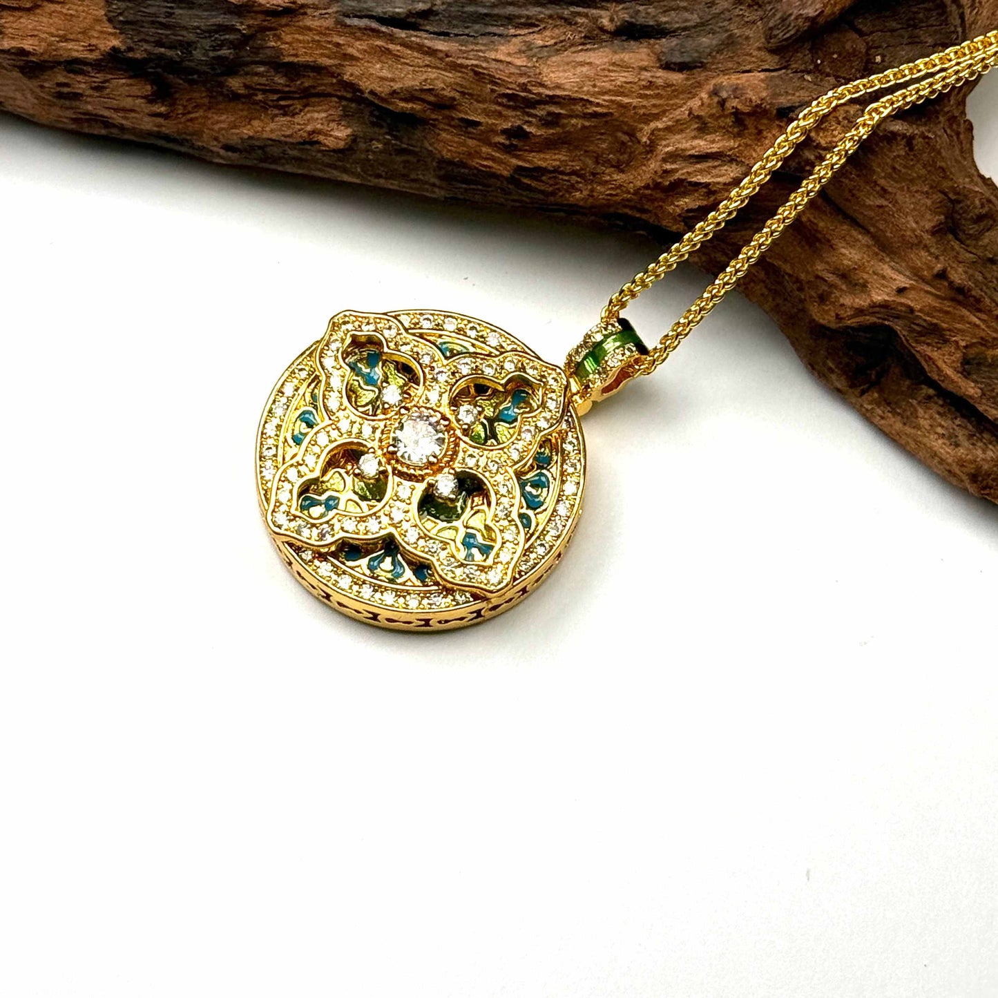 A regal sand gold sacred geometry mandala pendant with vibrant blue enamel accents and a gold wave chain, displayed elegantly against a rustic driftwood branch for a Zen look.
