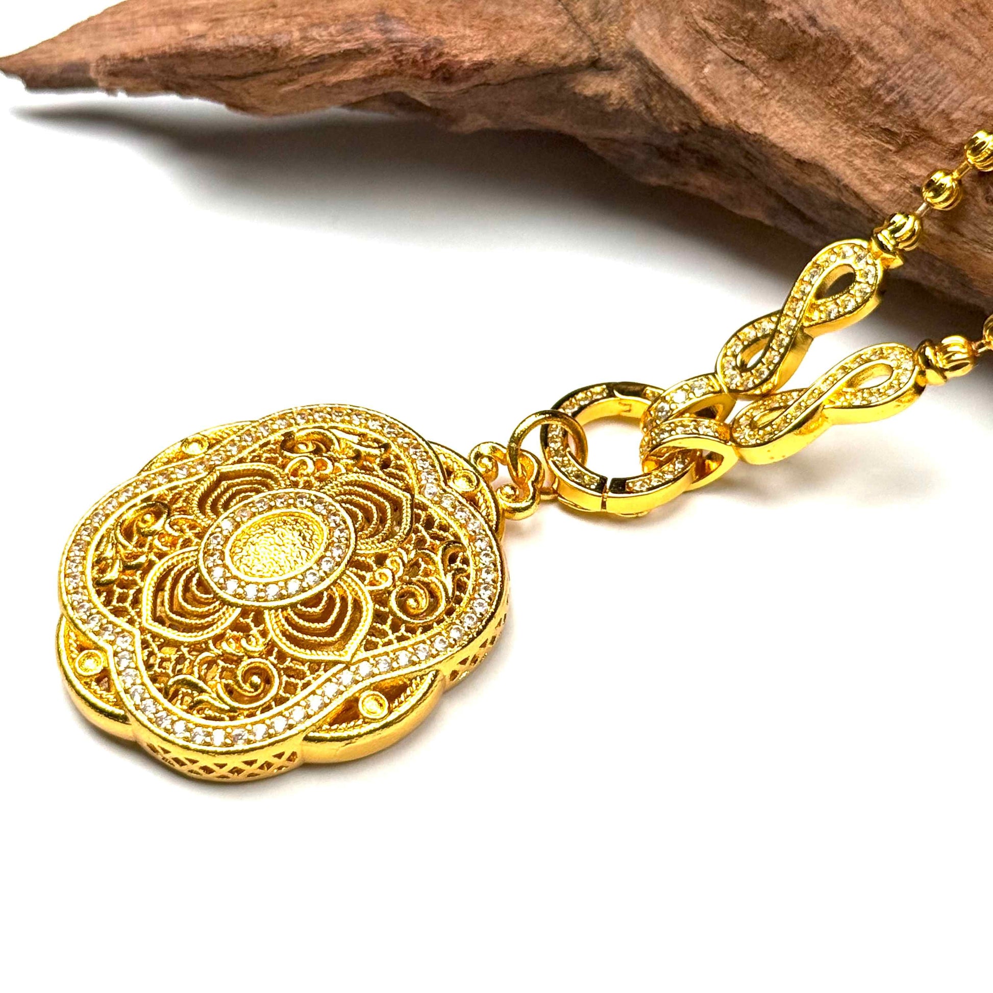 Macro top-down shot of a sand gold mandala locket charm, capturing the flawless pavé-set crystal border and interlocking gold clasp rings on wood.