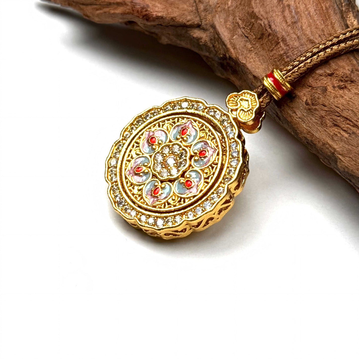 An elegant sand gold lotus spinner locket with pink enamel and crystals, resting gracefully on a piece of rustic wood for a Zen look.