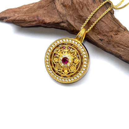 The embossed filigree back side of a golden spinning amulet displayed elegantly on a piece of natural rustic wood.