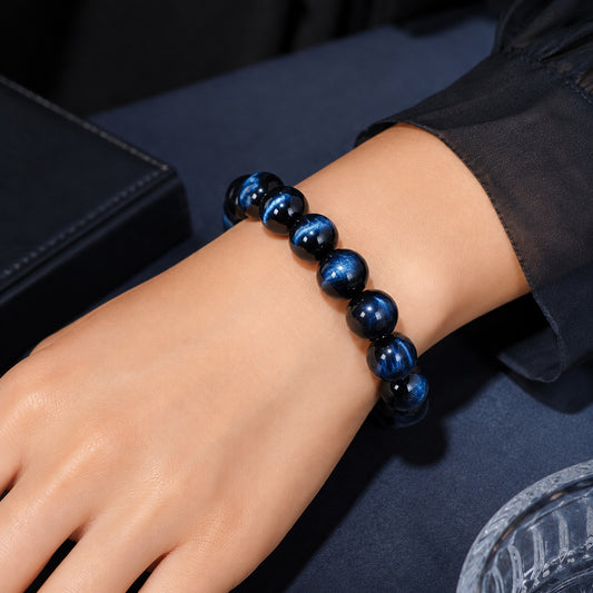 Luxury blue tiger’s eye bracelet worn on hand with dark satin background