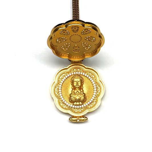 An opened traditional Buddhist prayer locket (Gau box) revealing a hidden golden seated Buddha inside, surrounded by rhinestones on a white backdrop.