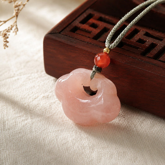 Close-up of a pink quartzite jade cloud pendant beside a wooden jewelry box