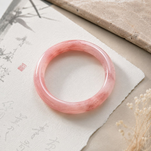 Top view of a polished pink quartzite jade bangle bracelet on a soft neutral background