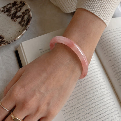 Close-up of a pink quartzite jade bangle bracelet worn on the wrist beside an open book
