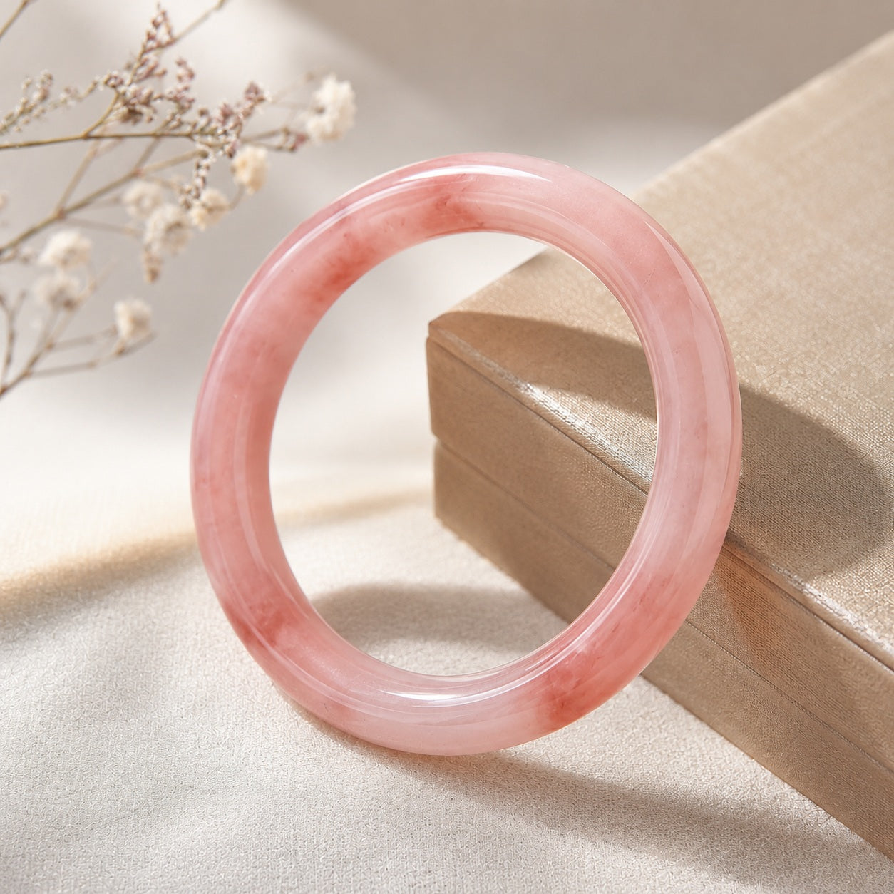 Pink quartzite jade bangle bracelet displayed beside a jewelry box in warm natural light