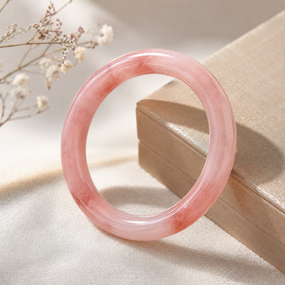Pink quartzite jade bangle bracelet displayed beside a jewelry box in warm natural light