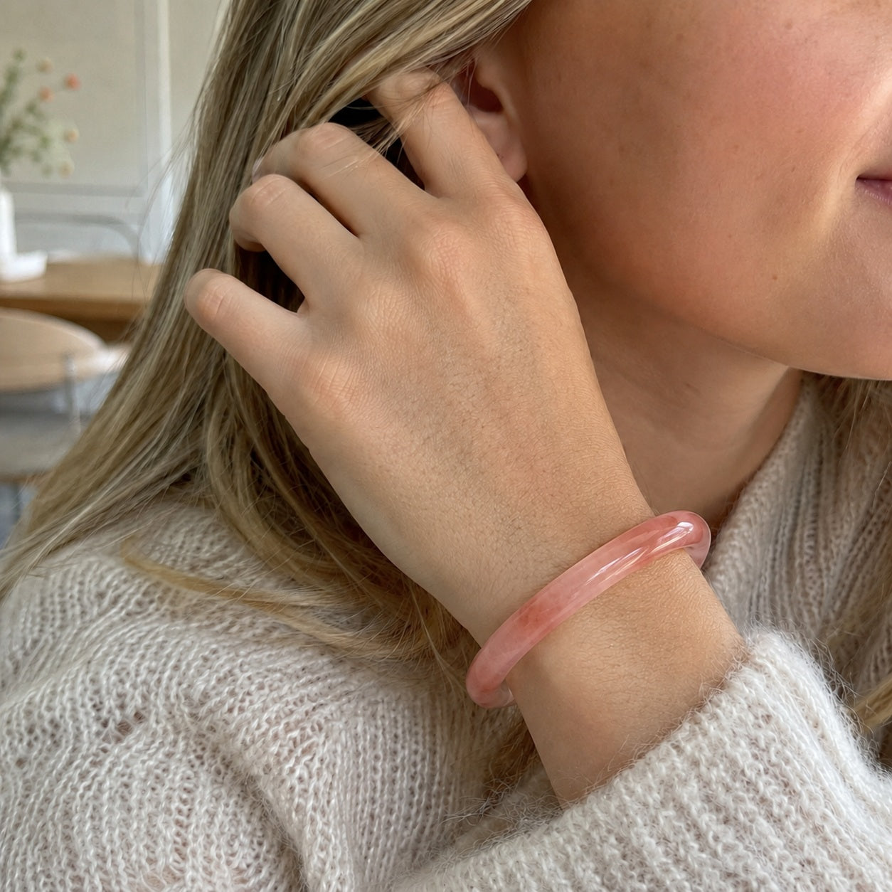 Woman wearing a soft pink quartzite jade bangle bracelet in a cozy neutral setting