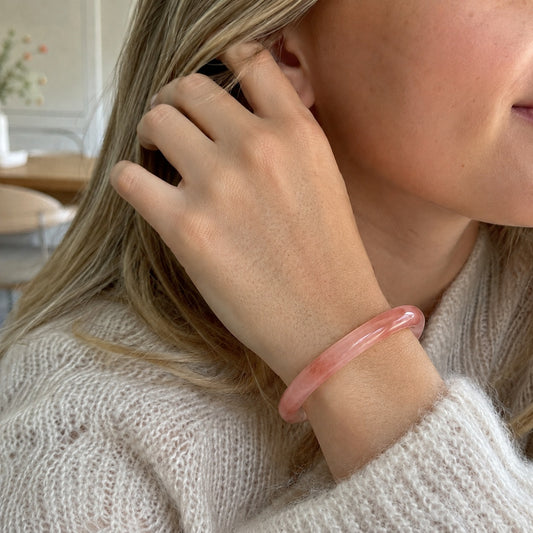 Woman wearing a soft pink quartzite jade bangle bracelet in a cozy neutral setting