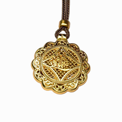 The reversible back side of a sand gold charm, showcasing deeply engraved Chinese characters for bringing in wealth and treasures on a delicate filigree mesh background.