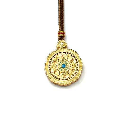 The reversible back side of a sand gold mandala pendant necklace, highlighting a central green gemstone and gold-tone embossed lotus petals.