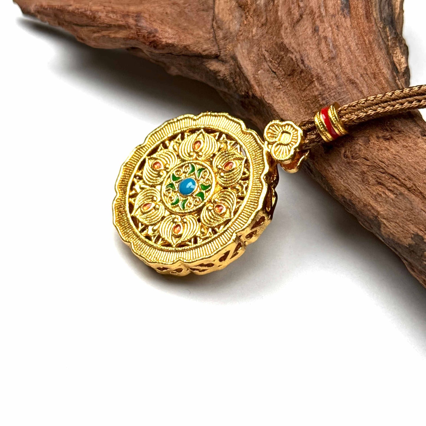 A Tibetan-style sand gold amulet pendant featuring a prominent green center stone, resting on natural driftwood background.