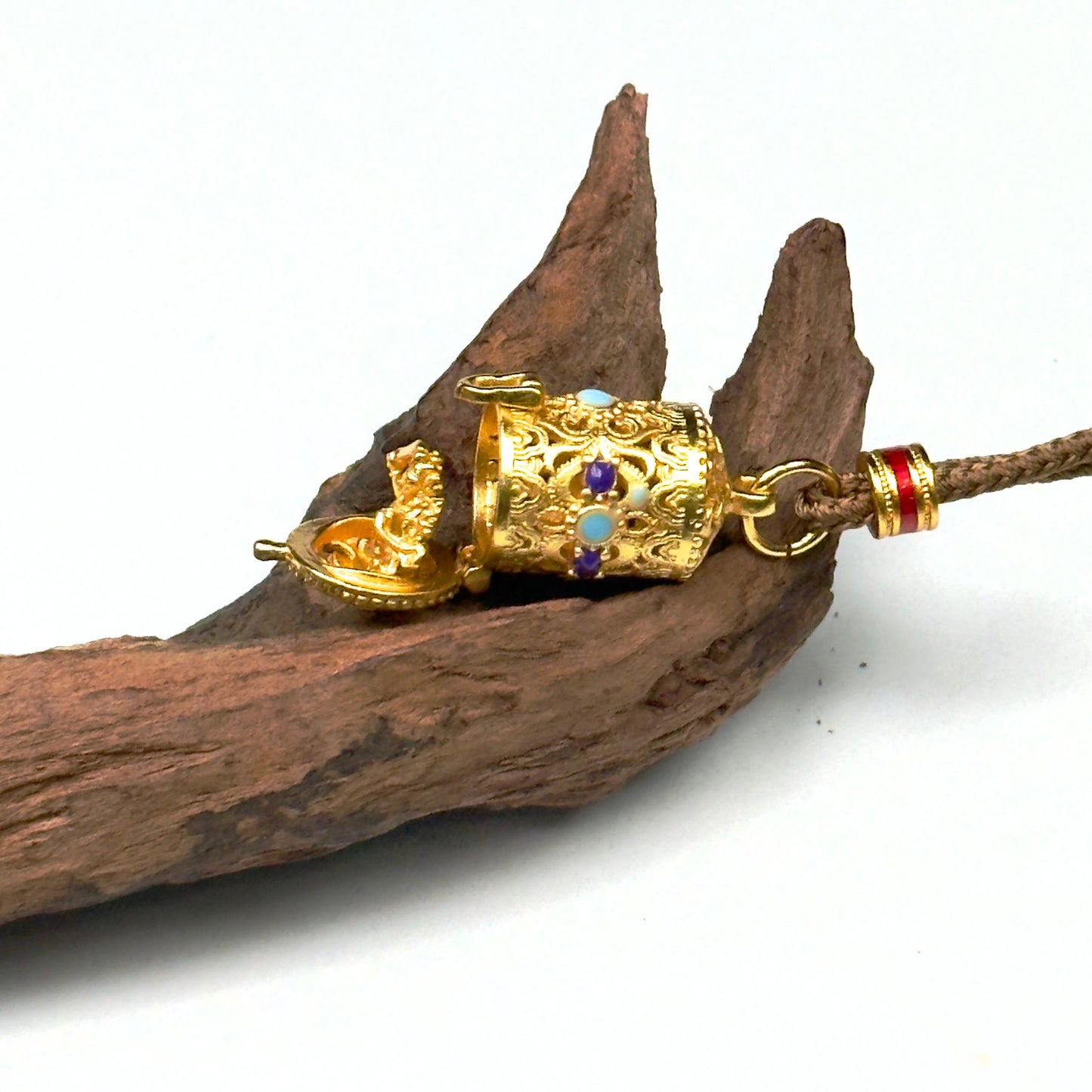 A horizontal shot of the opened sand gold protective capsule on wood, capturing the precise mechanical hinge and the embossed micro deity altar.