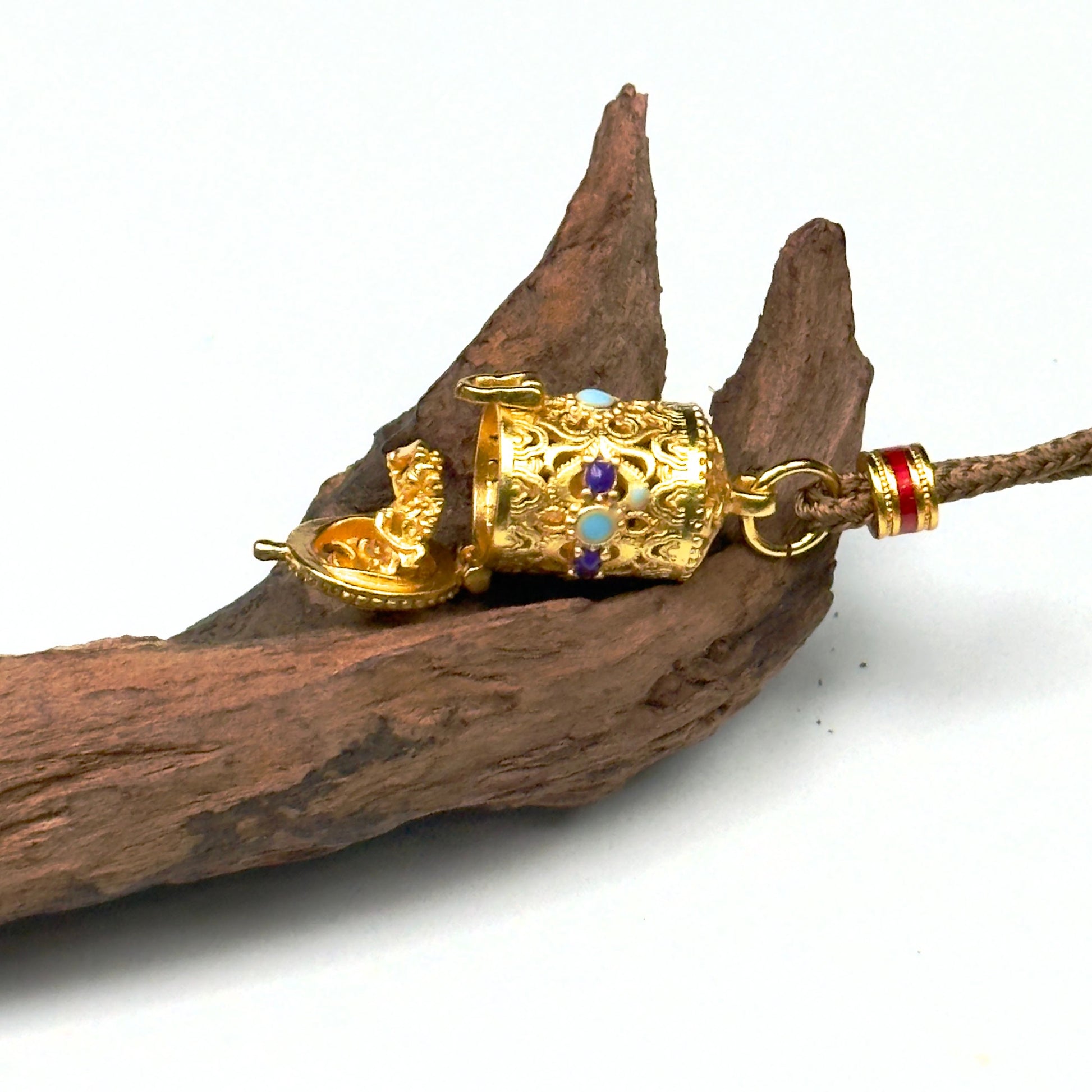 A horizontal shot of the opened sand gold protective capsule on wood, capturing the precise mechanical hinge and the embossed micro deity altar.