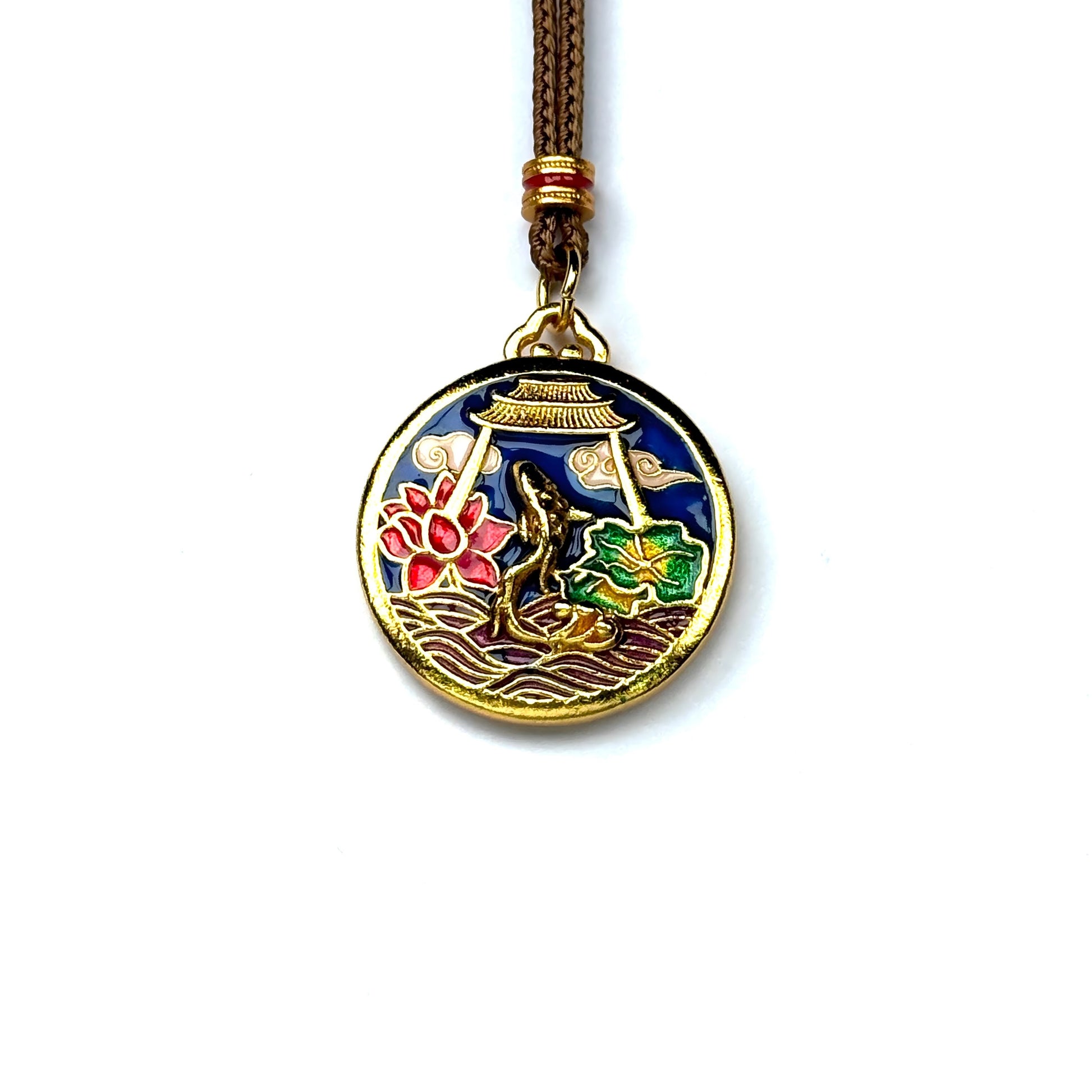 A front view of a round sand gold pendant featuring a vibrant enamel scene of a golden koi fish leaping near a pink lotus on a white background.