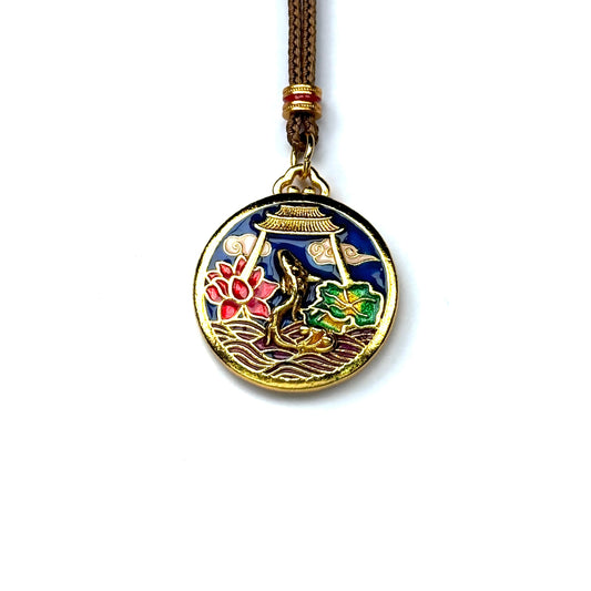 A front view of a round sand gold pendant featuring a vibrant enamel scene of a golden koi fish leaping near a pink lotus on a white background.