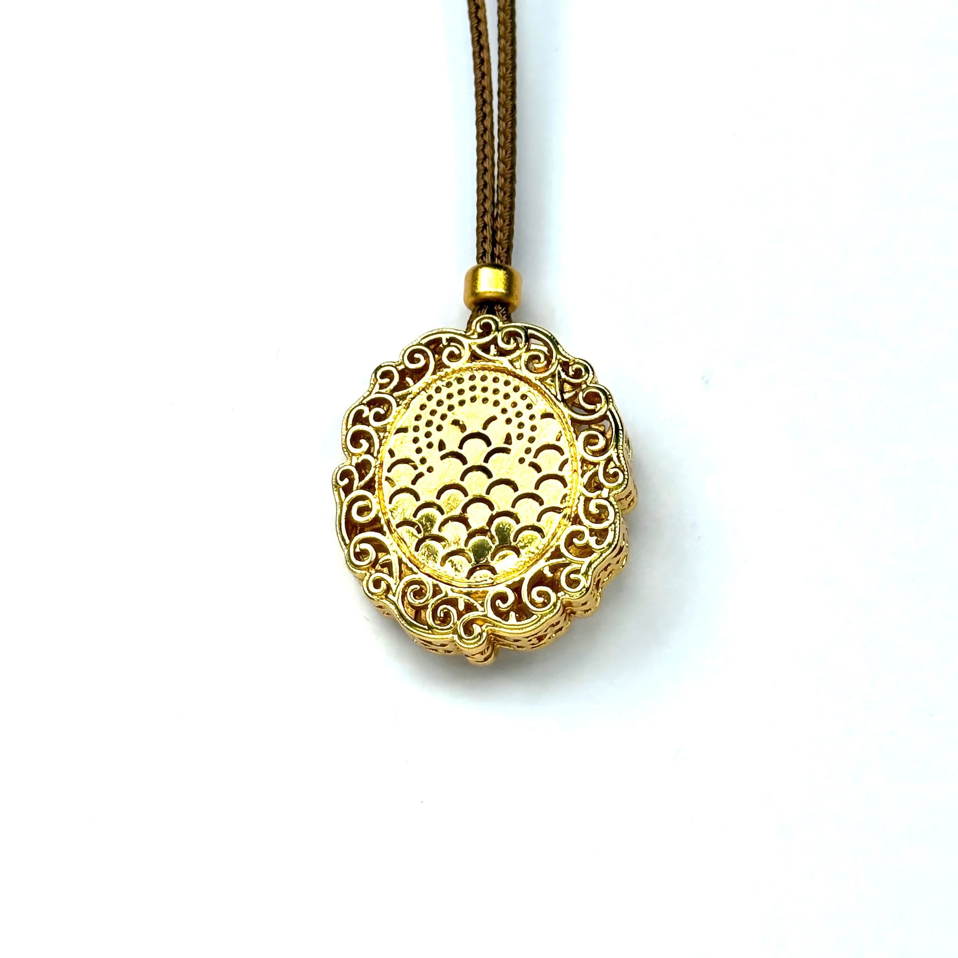 The finely engraved back side of a sand gold round pendant, showcasing a traditional fish scale geometric pattern on a white background.