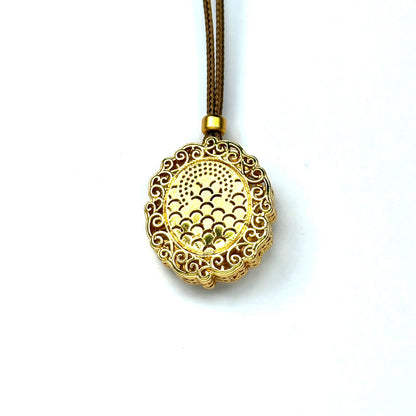 The finely engraved back side of a sand gold round pendant, showcasing a traditional fish scale geometric pattern on a white background.