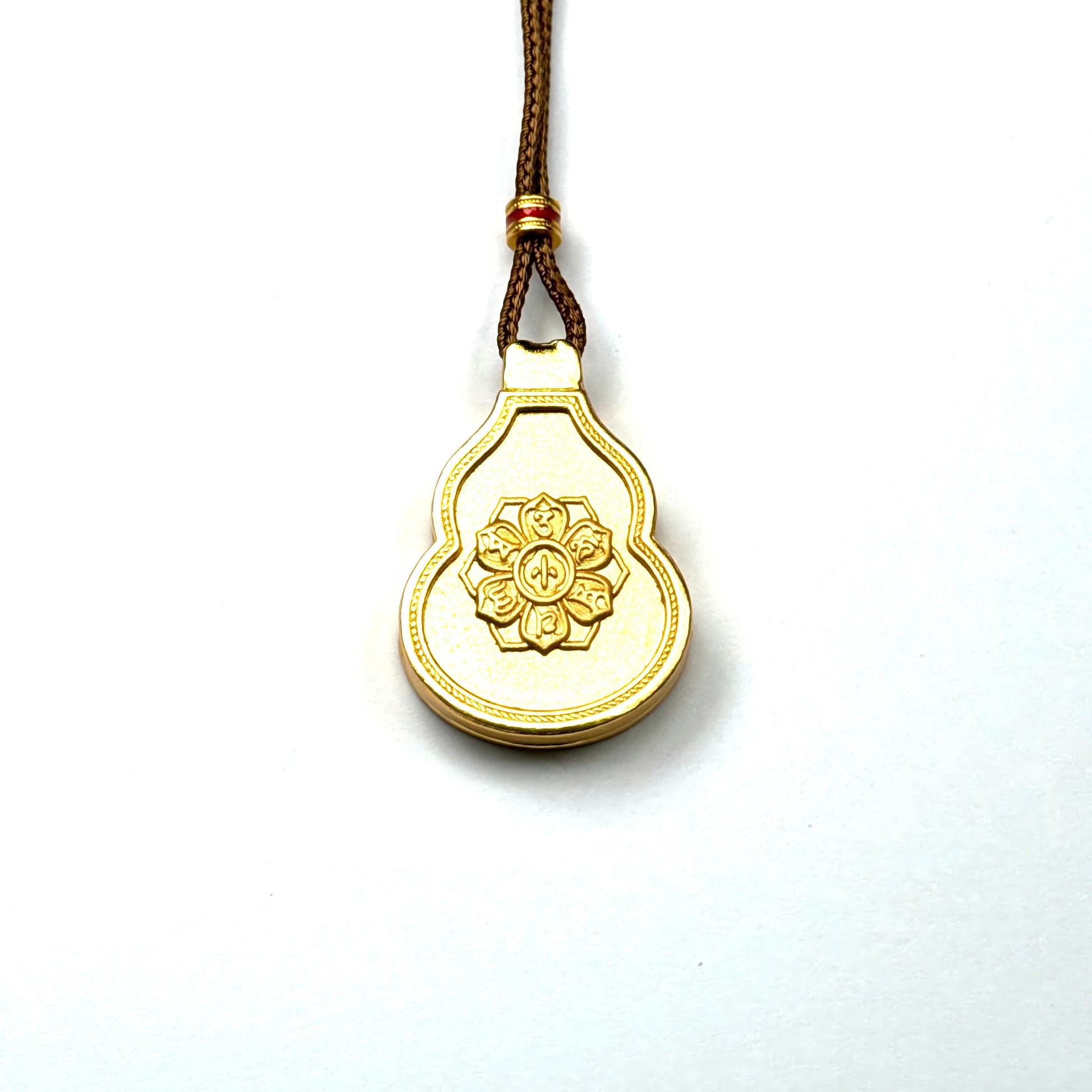 The back side of a sand gold gourd pendant, showcasing an engraved lotus flower and sacred Tibetan mantra script on a white background.