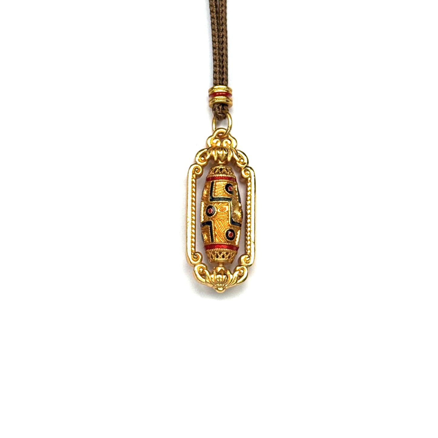 A front view of a gold-tone spinning Dzi bead pendant featuring intricate red and black enamel eye motifs inside an ornate golden frame on a white background.