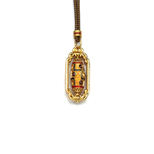 A front view of a gold-tone spinning Dzi bead pendant featuring intricate red and black enamel eye motifs inside an ornate golden frame on a white background.