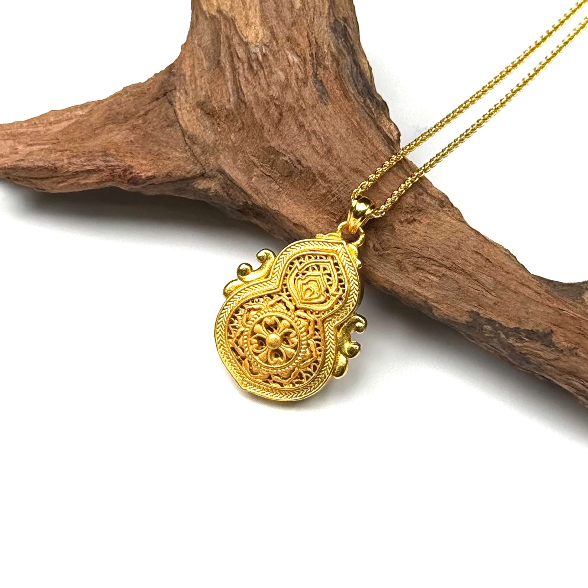 The beautifully textured filigree back side of a round sand gold gourd charm, capturing the flawless metallic shadows of the cross-vajra wheel symbol resting on wood.