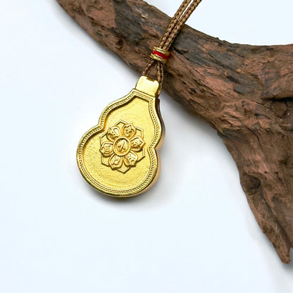 The beautifully brushed matte gold back side of a Hulu pouch charm displaying the sacred lotus blessing wheel on a natural driftwood background.