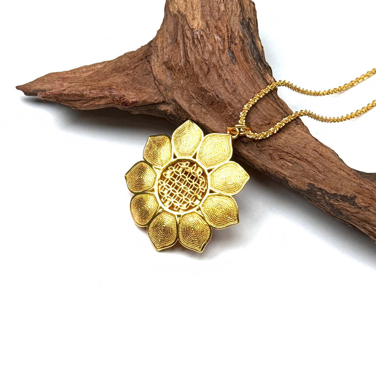 The embossed all-gold filigree back side of a blooming lotus charm necklace resting against natural rustic wood.