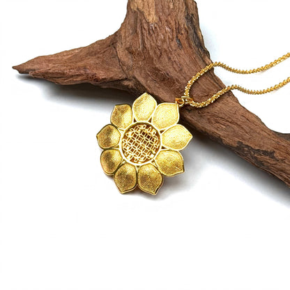 The embossed all-gold filigree back side of a blooming lotus charm necklace resting against natural rustic wood.