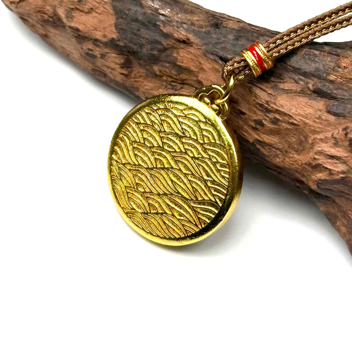 The embossed all-gold ocean wave back side of a round sand gold fortune talisman displayed elegantly on natural driftwood background.