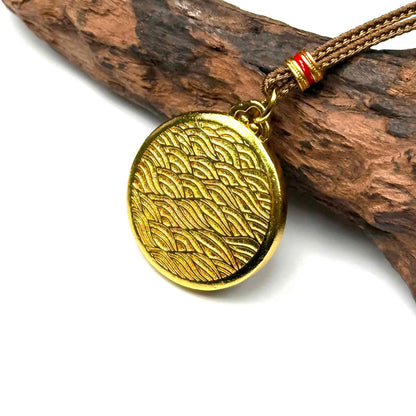 The embossed all-gold ocean wave back side of a round sand gold fortune talisman displayed elegantly on natural driftwood background.