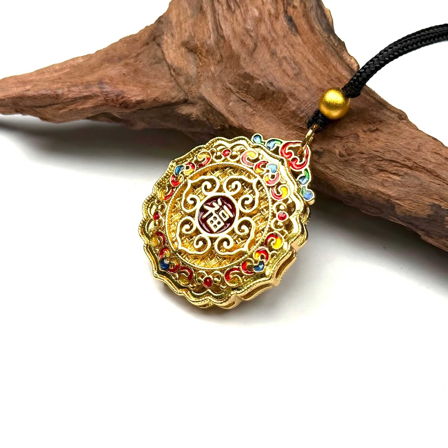 An elegant sand gold lotus rebirth pendant with vivid cloisonne-style enamel accents resting gracefully on a piece of rustic driftwood for a serene Zen look.